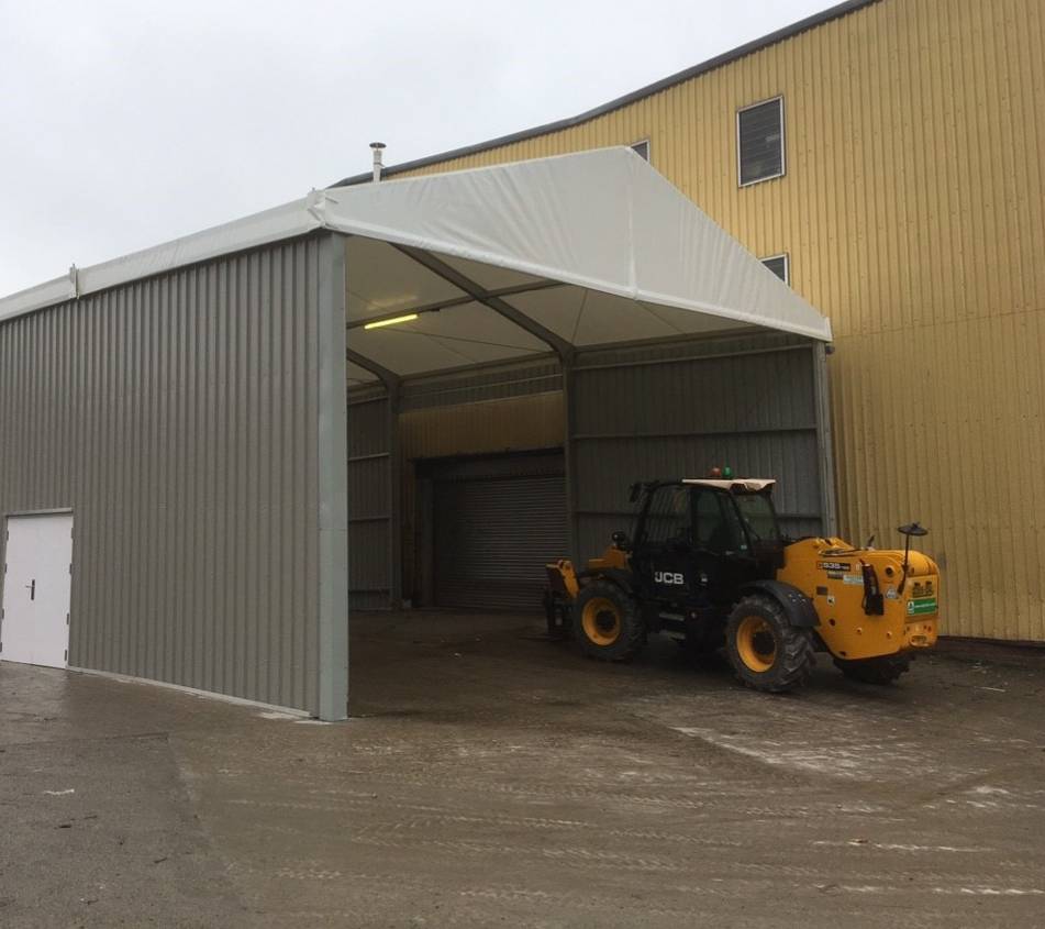 A temporary warehouse with a JCB digger driving underneath.